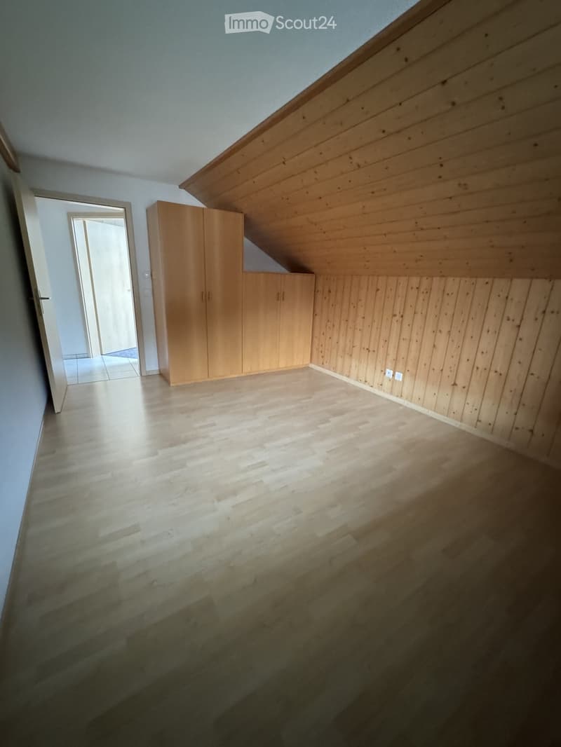 Empty attic room with wooden walls, wooden floor, and built-in wooden cabinetry. Slanted ceiling and open doorway visible.