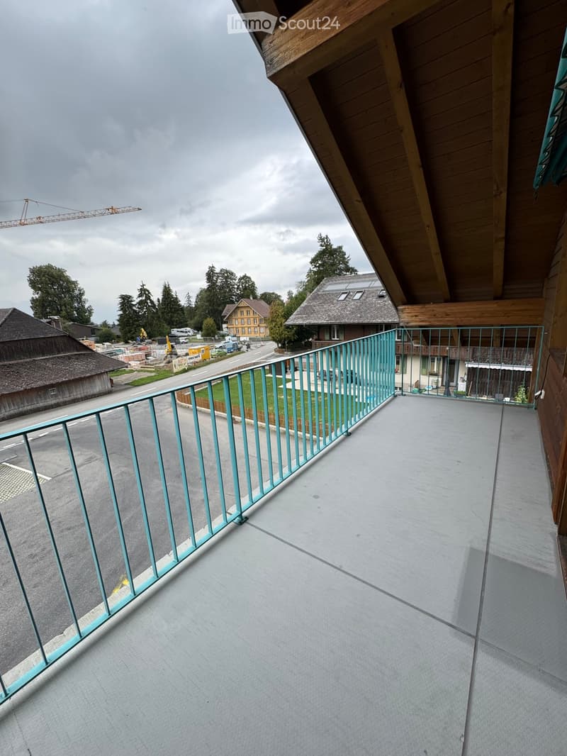 Balcony with a modern metal railing, overlooking a street with houses, trees, and construction activity.