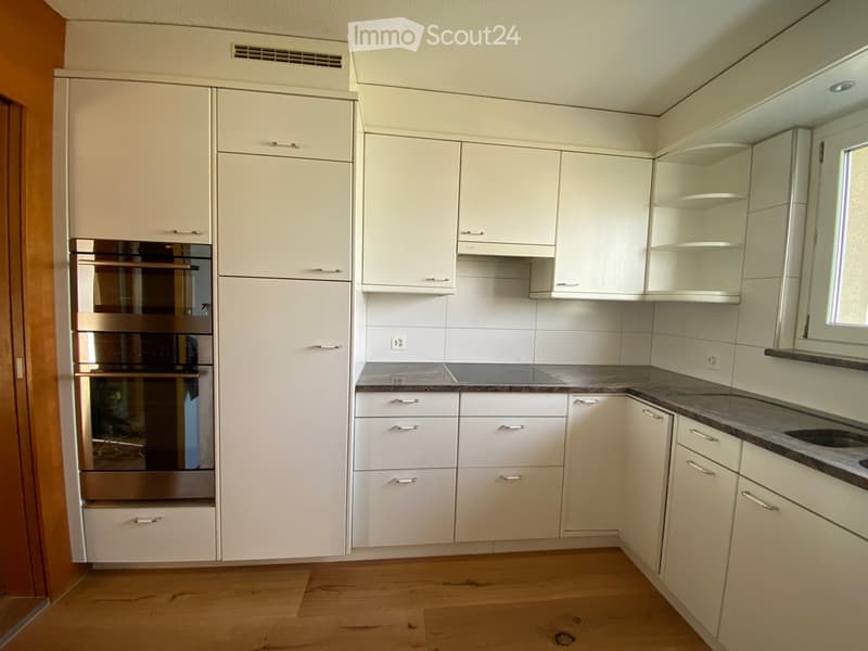 Modern kitchen with white cabinets, stainless steel oven, granite countertop, and wooden flooring.