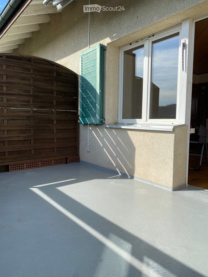 Balcony with a wooden lattice gate, a large window with shutters, and a concrete floor.