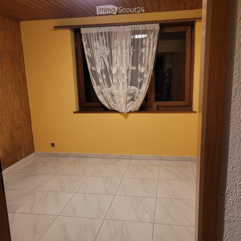 Empty room with yellow walls, tiled floor, and a window with sheer curtains.