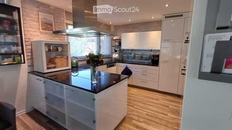 Modern kitchen with white cabinets, black countertops, stainless steel appliances, and a brick accent wall. Features include a microwave, refrigerator, oven, dishwasher, and a flower vase on the counter.