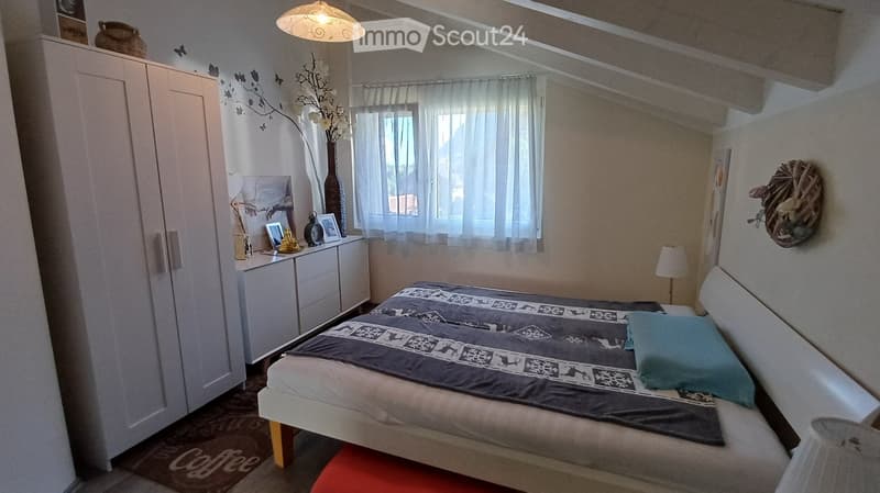 Cozy bedroom with a double bed, wardrobe, nightstand, lamp, and decorative items including a vase and wall art.