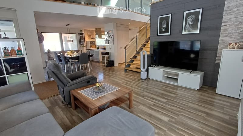 Modern living room with hardwood flooring, grey sofa, coffee table, TV, dining area with chairs and table, and a staircase leading to an upper level.