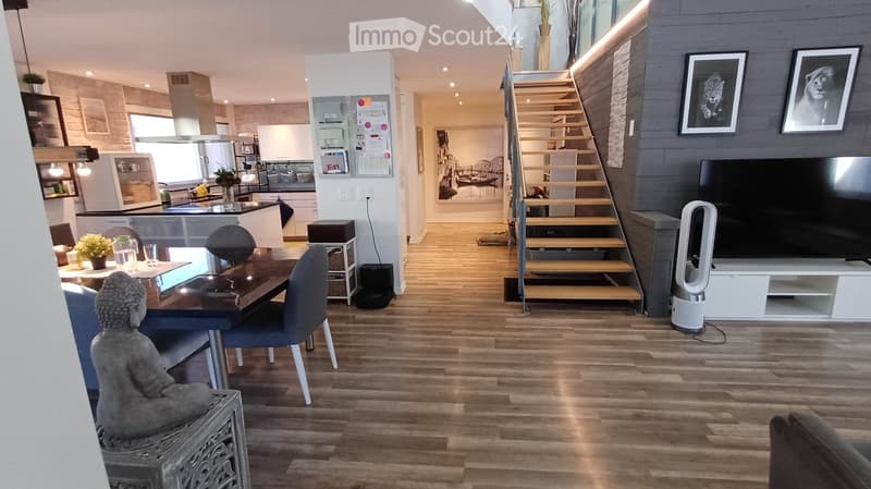 Open-plan living and dining area with wooden flooring, modern furniture, and a kitchen area in the background.