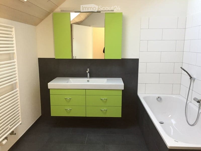 Modern bathroom with a white sink, green cabinets, a bathtub, and a mirror above the sink. The walls are tiled in black and white, and the floor is black.