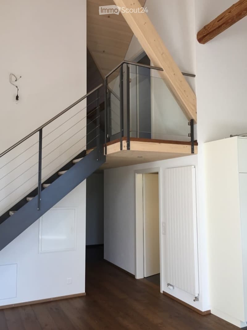 Modern hallway with wooden flooring, white walls, and a staircase leading to an upper level with glass railing and wooden balusters.