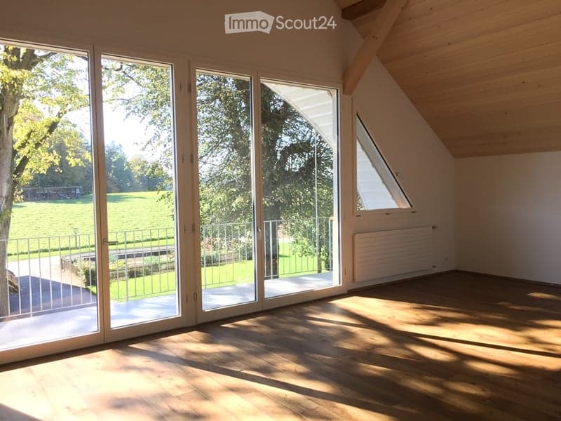 Bright, empty room with wooden flooring and large glass sliding doors leading to a garden. The room features a slanted wooden ceiling and a radiator on one wall.