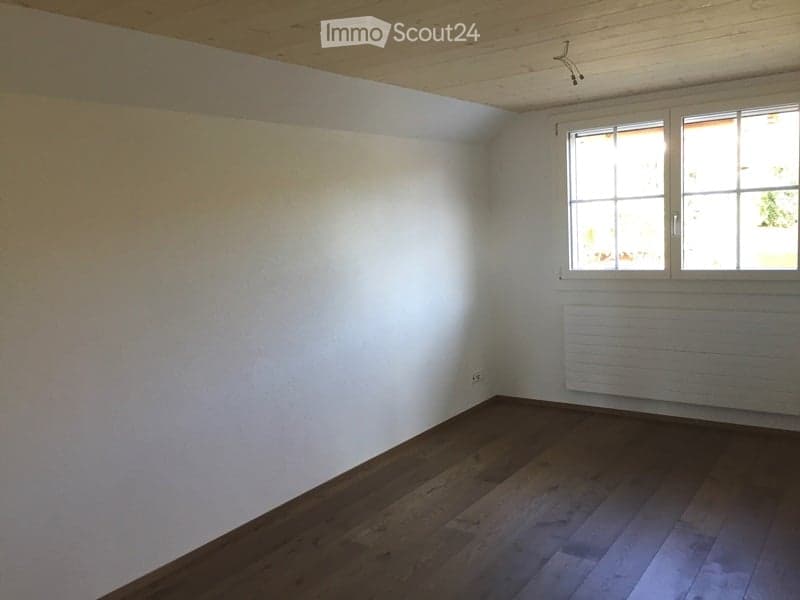 Empty room with wooden flooring, white walls, and a large window with white frames. A radiator is visible below the window.