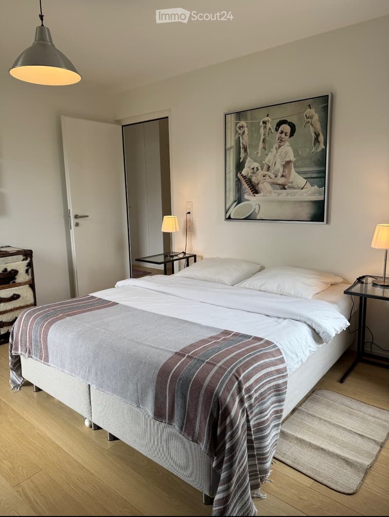 Modern bedroom with a large bed, nightstands, lamps, and a large picture frame on the wall.