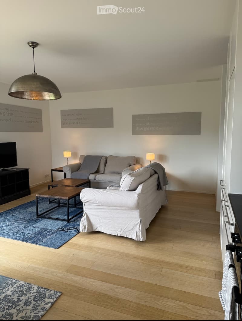 Modern living room with light wooden flooring, a grey sofa, a white armchair, a coffee table, a television, and decorative wall art.