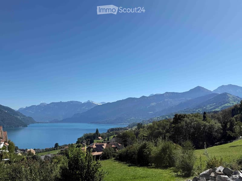 Scenic view of a lake surrounded by mountains, with a small village and green fields in the foreground.