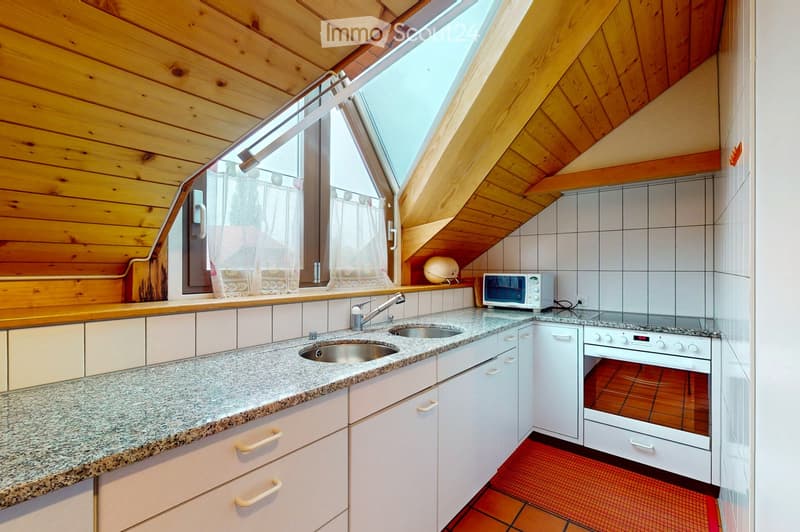 Modern kitchen with white cabinets, granite countertop, double sink, and stainless steel appliances including an oven and microwave. Wooden ceiling and large skylight provide natural light.