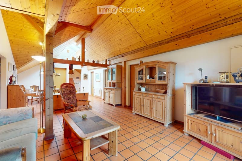 A spacious living room with exposed wooden beams, tiled flooring, and a mix of modern and traditional furniture including a sofa, coffee table, armchair, cabinet, and television.