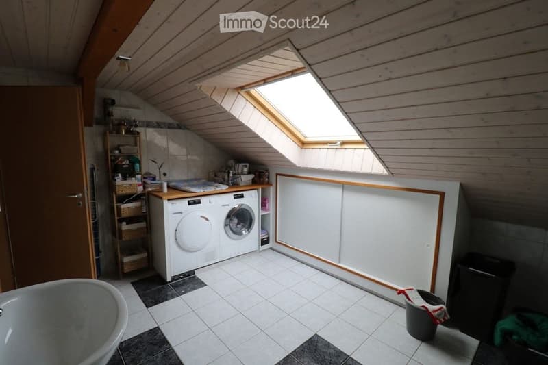 Bright attic bathroom with skylights, white tiled floor, bathtub, washing machine, dryer, and built-in cabinets.