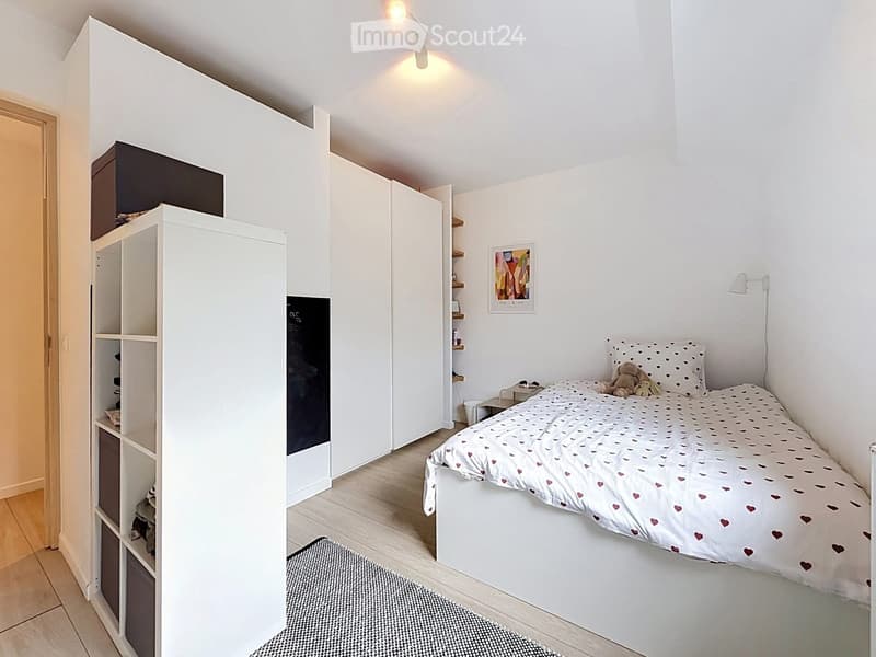 Modern bedroom with a white bed, heart-patterned bedding, a large white wardrobe, shelves, and a nightstand.
