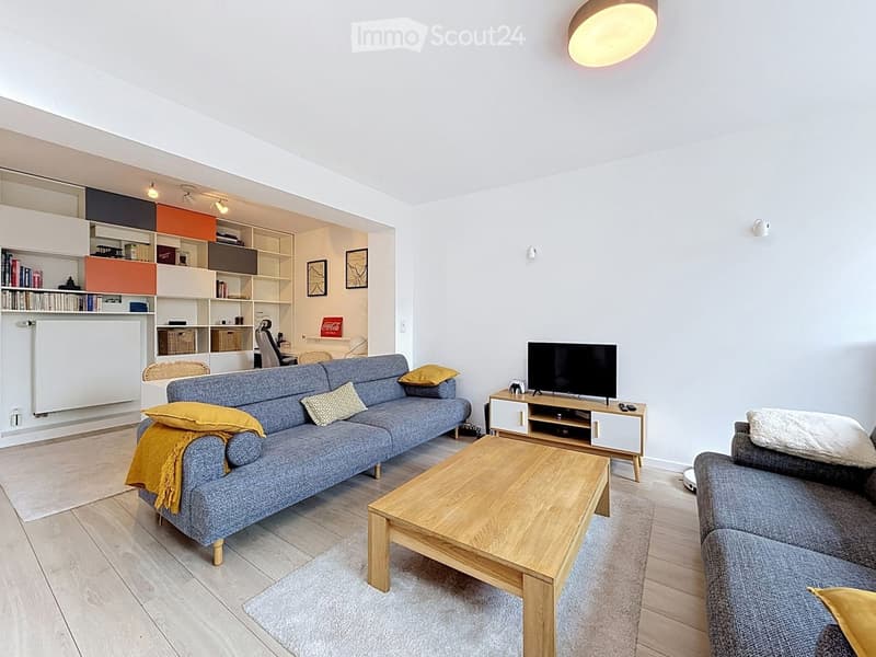 Modern living room with a grey sofa, wooden coffee table, TV stand, and shelves in the background.