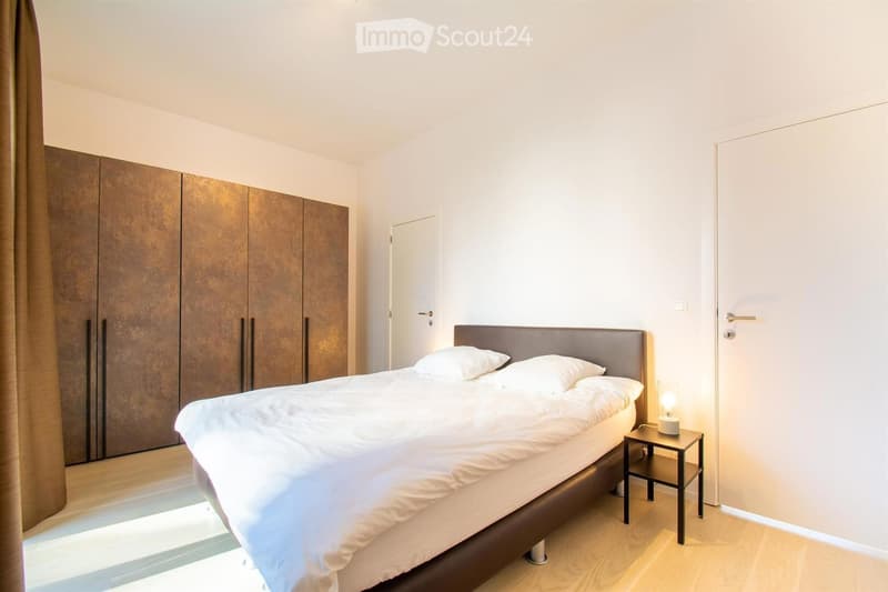Modern bedroom with a large bed, nightstand, lamp, and a large wardrobe with wooden doors.