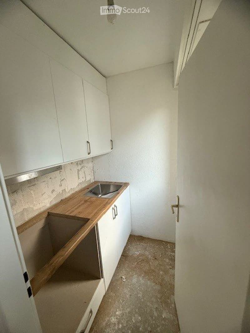 Empty kitchen with white cabinets, wooden countertop, and a sink. No appliances or furniture present.