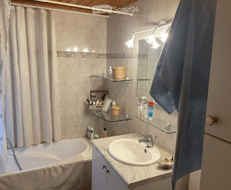 Bathroom with a bathtub, sink, mirror, shelves, and various toiletries including a towel, toothbrush, toothpaste, shampoo, and soap.