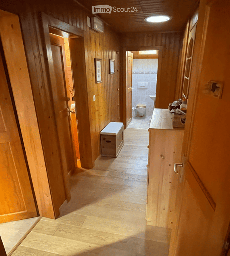Wooden-paneled hallway with a bench, leading to a bathroom with a toilet and sink.