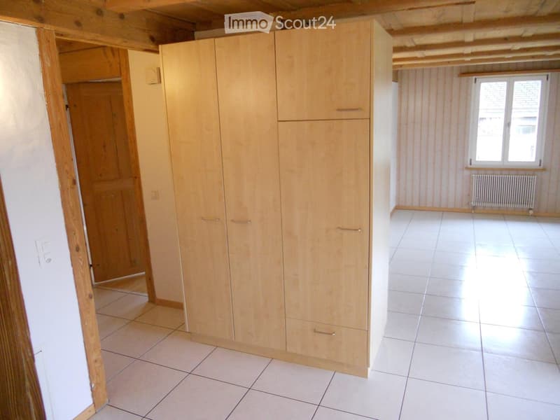 Empty room with tiled floor, wooden built-in wardrobe, and a window with radiator below it.