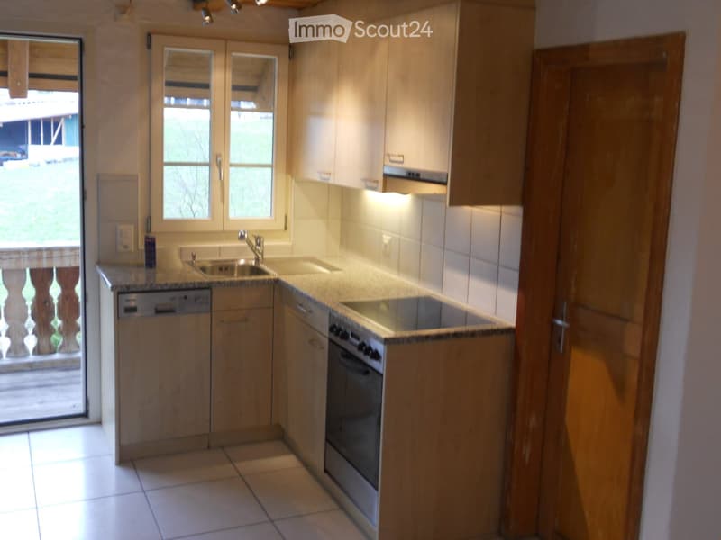 Modern kitchen with light wooden cabinets, granite countertops, stainless steel sink, oven, and dishwasher. Features a window with blinds and a door leading outside.