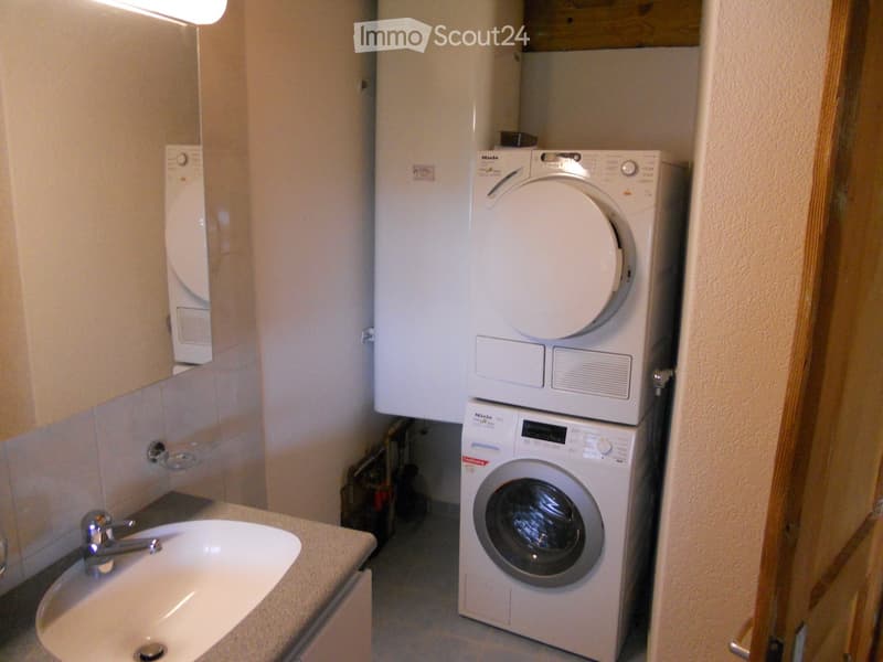 Compact bathroom with a sink, stacked washing machine and dryer, and tiled walls.