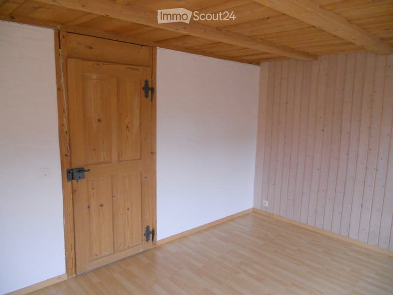 Empty room with wooden floor, light-colored walls, and a wooden door with metal hardware.