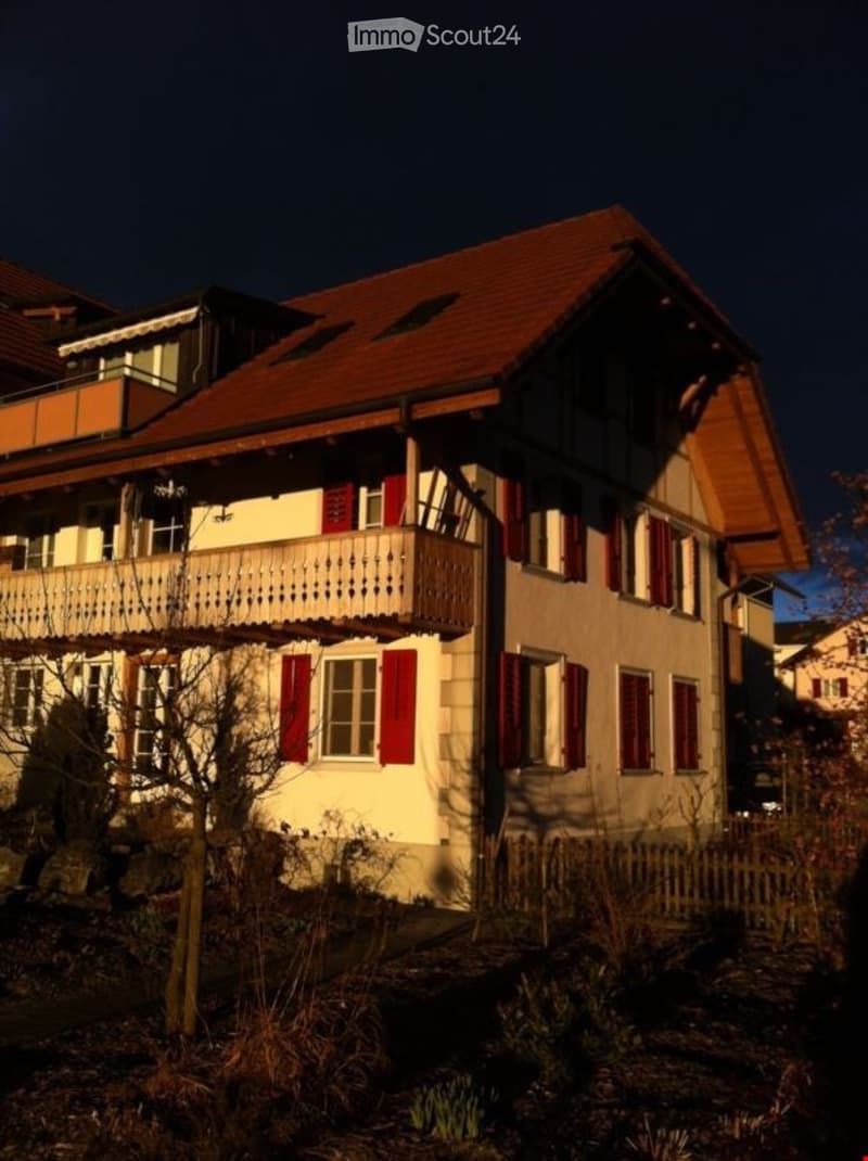 Two-story house with red shutters, a balcony, and a well-maintained garden.