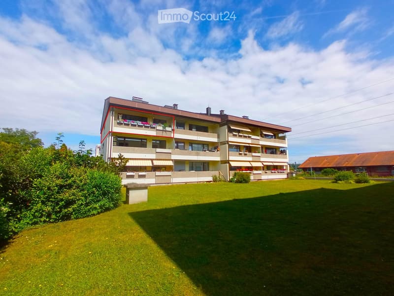 A multi-story residential building with balconies, surrounded by a well-maintained lawn and greenery.