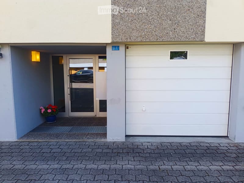 Entrance to a building with a garage door, glass double doors, and a small flower pot on the left side.