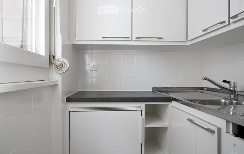 Modern kitchen with white tiled walls, white cabinets, a black countertop, and a stainless steel sink with a modern faucet.