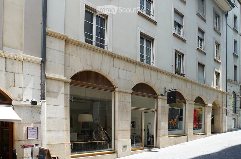 Classic European building facade with arched windows and doors, featuring a storefront with glass display windows and a small outdoor seating area.