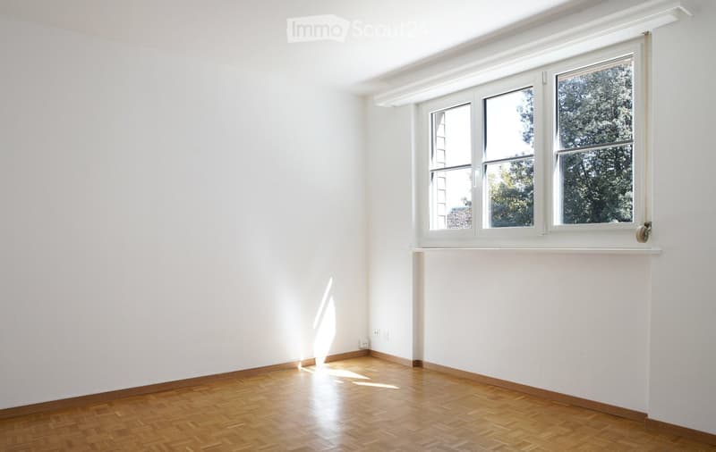Empty room with white walls, wooden floor, and large windows with white frames. No furniture or equipment present.