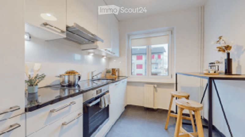 Modern kitchen with white cabinets, stainless steel appliances, a stove, oven, sink, and a small table with stools.