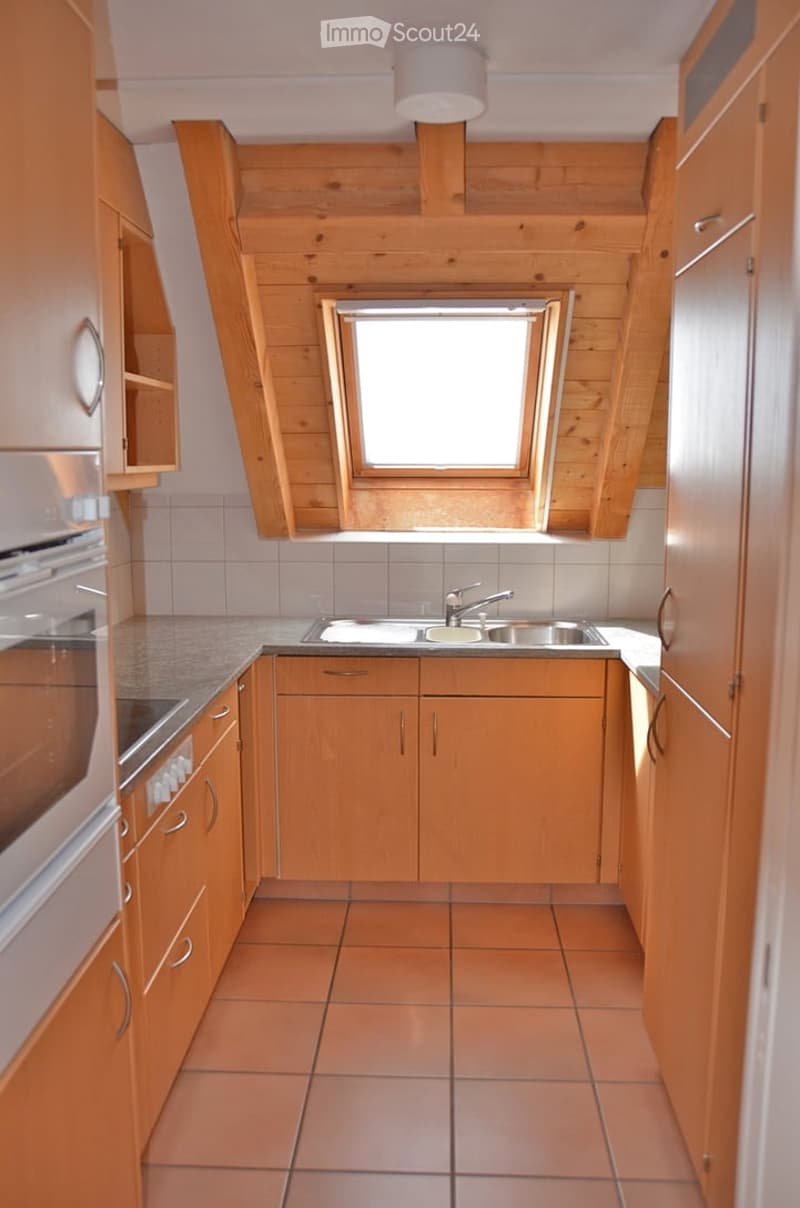 Bright kitchen with wooden cabinets, tiled floor, and a window above the sink.