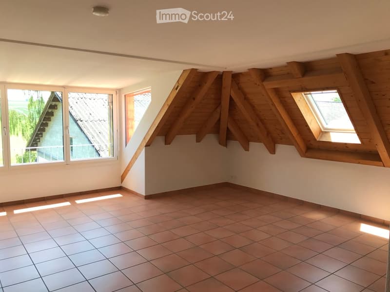 Empty attic room with exposed wooden beams, tiled floor, and multiple windows allowing natural light.