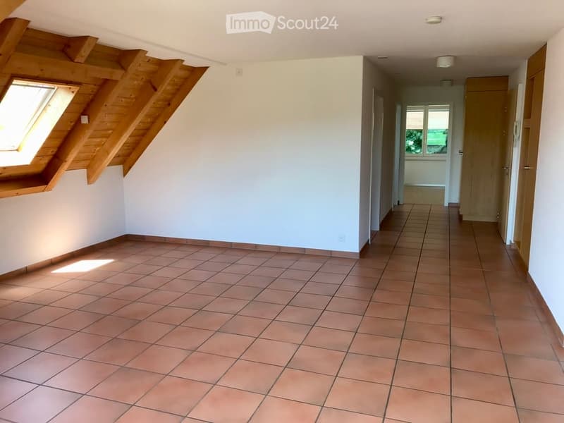 Empty room with tiled floor, white walls, and wooden beams on the ceiling. A window with wooden frame is visible on the left side.