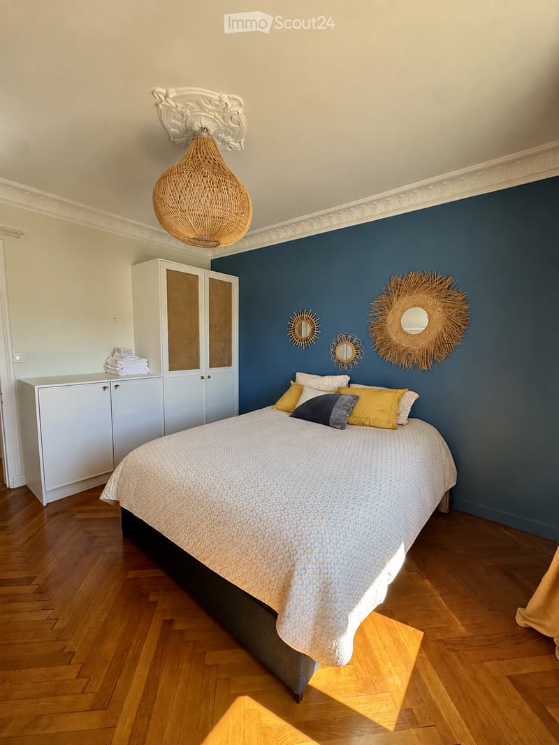Elegant bedroom with a large bed, multiple pillows, a white wardrobe, decorative mirrors, and a woven pendant light.