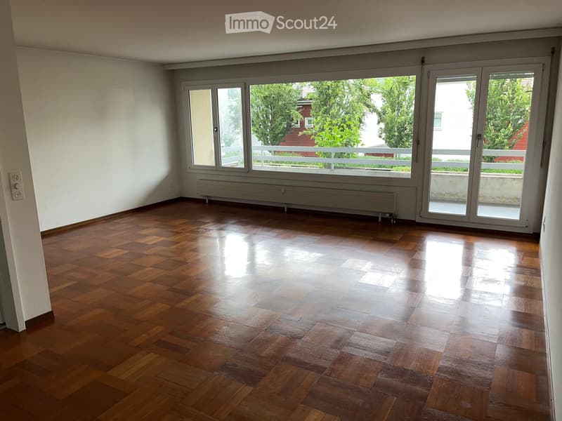 Empty room with wooden flooring, large windows, and sliding glass doors leading to a balcony.