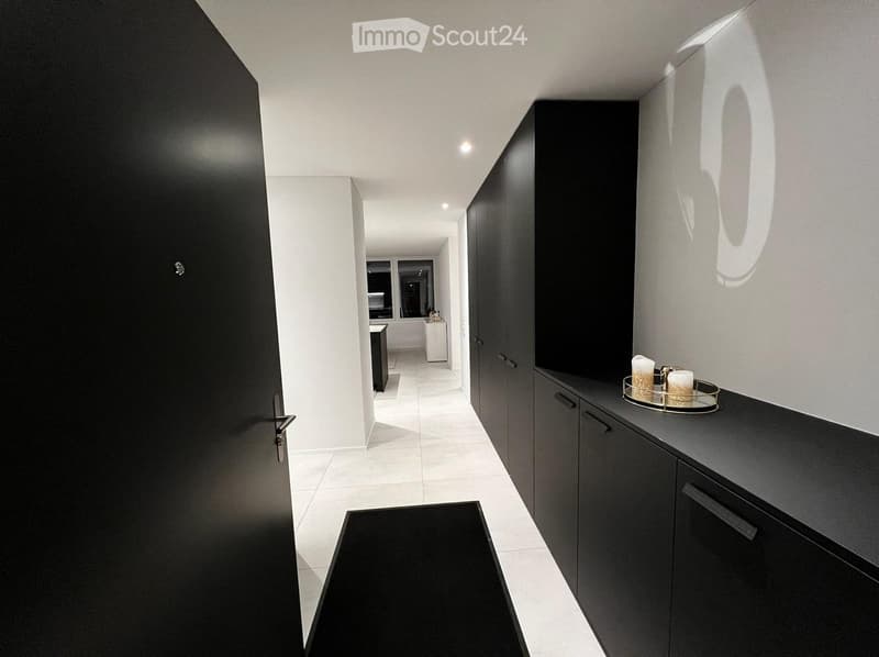 Modern hallway with sleek black cabinets, white walls, and a polished tile floor. A small decorative tray with candles is placed on a black countertop to the right.
