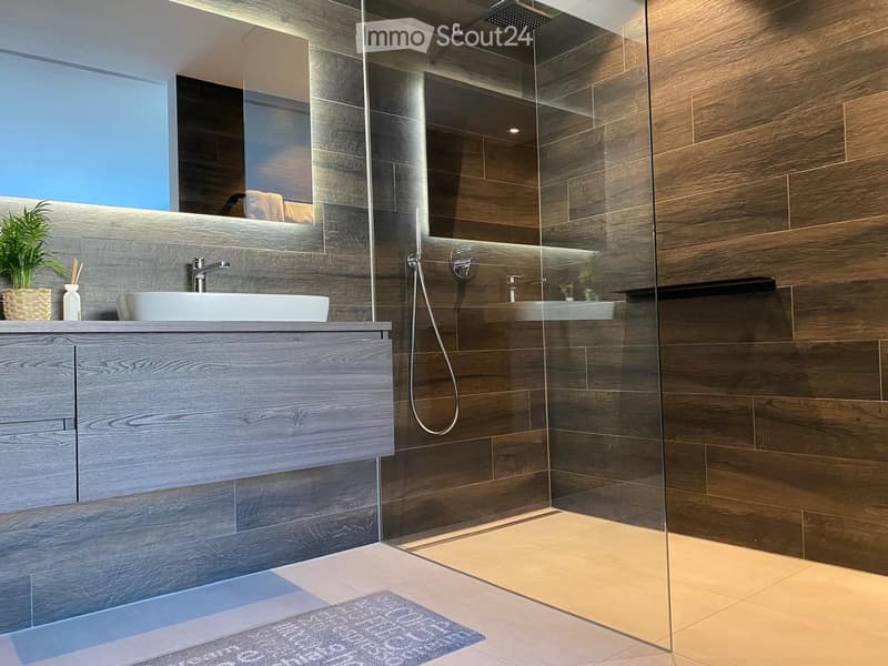 Modern bathroom with a wooden vanity, white sink, glass shower enclosure, and a large mirror above the sink.