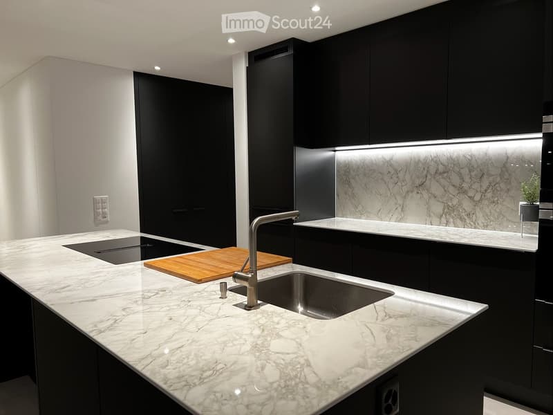 Modern kitchen with marble countertops, black cabinets, a sink, and a cutting board on the counter.