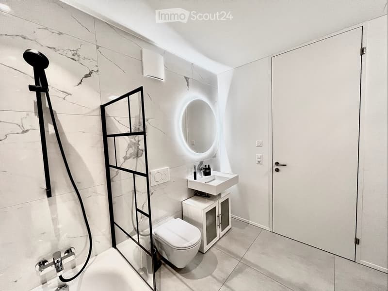 Modern bathroom with marble walls, a white sink, toilet, and a shower area with a glass partition and a black shower head.