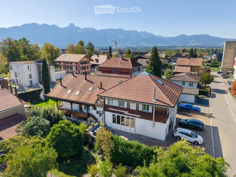 Aerial view of a residential neighborhood with multiple houses, red-tiled roofs, and surrounding greenery, with mountains in the background.