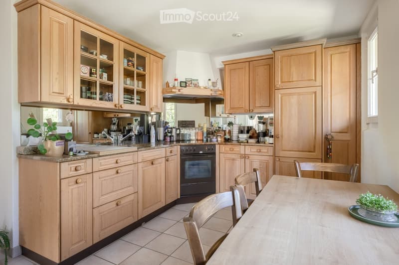 Bright kitchen with light wooden cabinets, granite countertops, and stainless steel appliances. Includes a dining area with a wooden table and chairs.