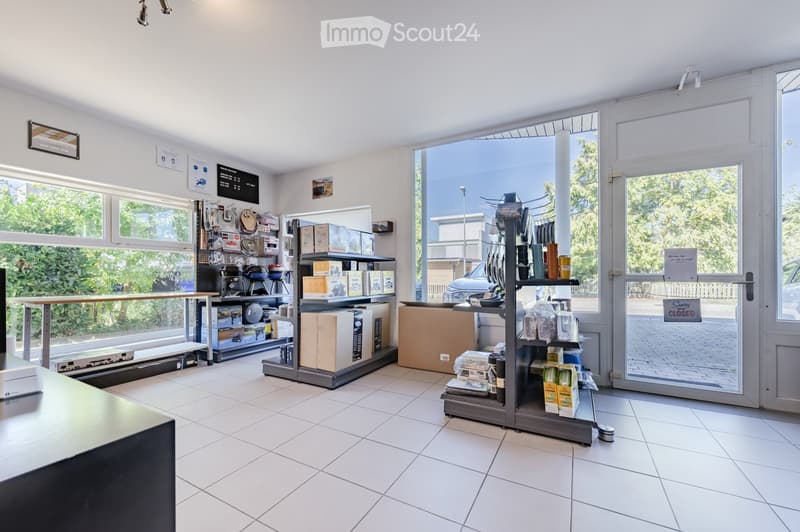 Bright, organized retail or storage space with large windows, tiled floor, shelves filled with boxes and products, and a counter on the left side.