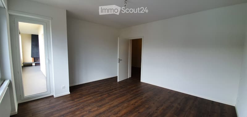 Empty room with wooden flooring, white walls, and two open doors leading to adjacent spaces.