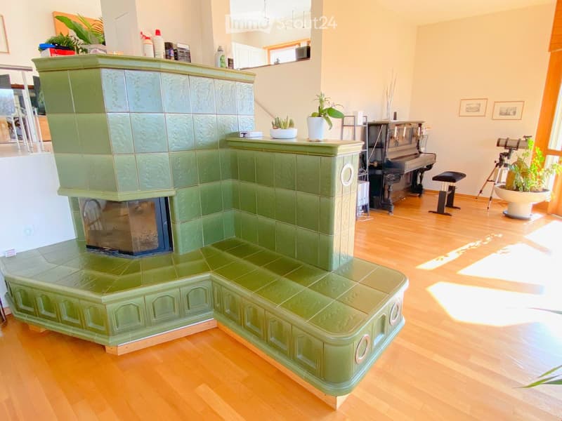 Living room with a green tiled fireplace, wooden floor, piano, tripod, and potted plants.